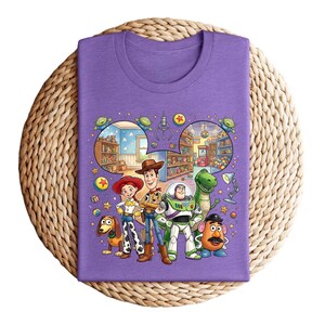 Pode incluir: Uma camiseta roxa com um gr&aacute;fico colorido dos personagens de Toy Story. O design apresenta Woody, Buzz Lightyear, Jessie, Rex, Sr. Batata, Slinky Dog e outros elementos do filme de anima&ccedil;&atilde;o.