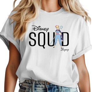 Puede incluir: Camiseta blanca con la frase "Disney Squad" y una ilustraci&oacute;n de dibujos animados de Bo Peep. El dise&ntilde;o incluye el nombre de Bo Peep. Las mangas de la camiseta est&aacute;n enrolladas.