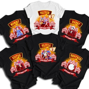May include: A collection of five black t-shirts and one white t-shirt featuring circus-themed graphics. Each shirt displays a carnival tent, a character, and text including Mommy, Daddy, Sister, Brother, Oliver, and Olivia with the number 5.