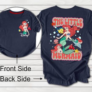 May include: Navy blue t-shirt featuring a front graphic of Ariel from Disney's The Little Mermaid, with the Disney logo. The back of the shirt displays a larger graphic with the text "The Little Mermaid" and Ariel with other characters.