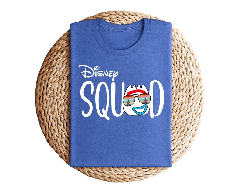 Puede incluir: Una camiseta azul con la frase "Disney Squad" en blanco. La "O" de "Squad" se reemplaza con un personaje de dibujos animados con gafas de sol. La camiseta est&aacute; doblada y colocada sobre una estera circular tejida.