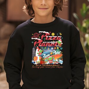 May include: Black sweatshirt with a Christmas-themed Pizza Planet design. It features a rocket, a Christmas tree, and three alien characters. The text reads "Pizza Planet" and "Out of this world quality. Serving your local star cluster."