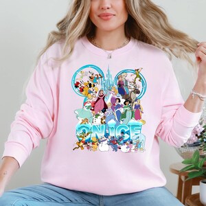 Puede incluir: Sudadera rosa con un estampado gr&aacute;fico de personajes de Disney, incluyendo Mickey Mouse, Minnie Mouse, Donald Duck, Goofy y otros. El gr&aacute;fico es un dise&ntilde;o de orejas de Mickey Mouse azul y blanco con la palabra "NICE" escrita debajo.