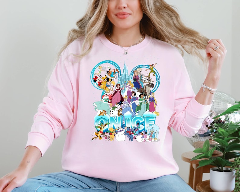 Puede incluir: Sudadera rosa con un estampado gr&aacute;fico de personajes de Disney, incluyendo Mickey Mouse, Minnie Mouse, Donald Duck, Goofy y otros. El gr&aacute;fico es un dise&ntilde;o de orejas de Mickey Mouse azul y blanco con la palabra "NICE" escrita debajo.