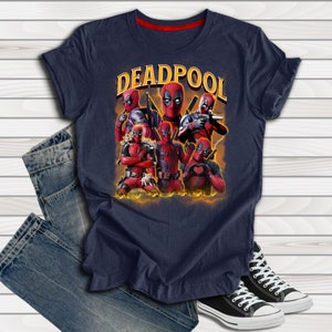 May include: A navy blue t-shirt with a graphic print of Deadpool characters in red and black. The text "DEADPOOL" is printed in yellow above the graphic.