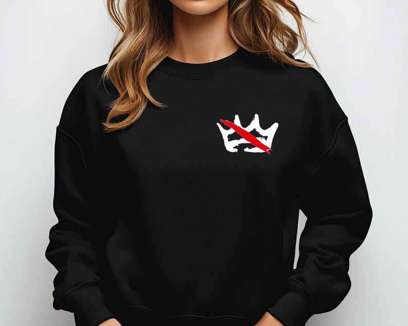 Peut inclure: Sweat-shirt noir avec un motif de couronne blanche barr&eacute;e d'une ligne rouge sur le c&ocirc;t&eacute; gauche de la poitrine. Le sweat-shirt a un col rond et des manches longues. Le motif est un graphisme audacieux.
