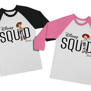 Puede incluir: Dos camisetas ragl&aacute;n blancas con mangas negras y rosas. Cada camiseta tiene el texto "Disney SQUAD" en negro, con una ilustraci&oacute;n de personaje de dibujos animados. Una camiseta presenta a Woody, la otra a Jessie.
