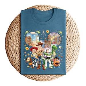 Pode incluir: Camiseta azul-petr&oacute;leo com um gr&aacute;fico colorido de personagens do filme Toy Story. O design inclui Woody, Buzz Lightyear, Jessie, Rex, Sr. Batata e Slinky Dog, com um fundo de loja de brinquedos.