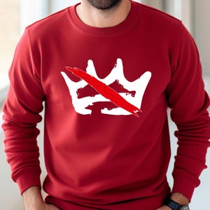 Peut inclure: Un sweat-shirt rouge avec un motif de couronne blanche barr&eacute;e d'une ligne rouge. Le motif est centr&eacute; sur la poitrine. Le sweat-shirt a des manches longues et un col rond.