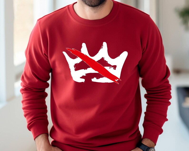 Peut inclure: Un sweat-shirt rouge avec un motif de couronne blanche barr&eacute;e d'une ligne rouge. Le motif est centr&eacute; sur la poitrine. Le sweat-shirt a des manches longues et un col rond.