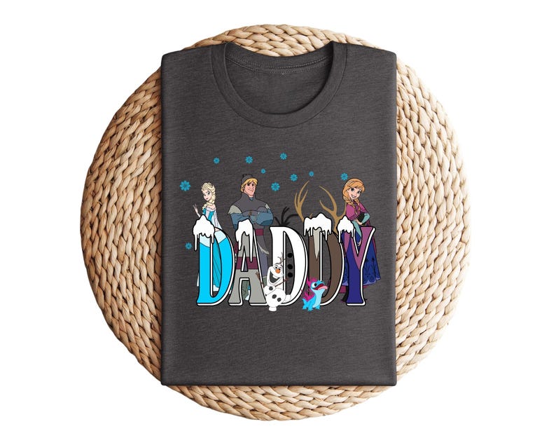 May include: A dark gray t-shirt featuring the word "DADDY" in a stylized font with characters from the movie Frozen. The letters are decorated with images of Elsa, Anna, Kristoff, Olaf, and Sven. Blue snowflakes are scattered above the letters.