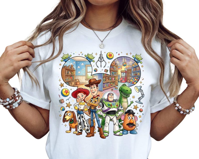 Pode incluir: Camiseta branca com um gr&aacute;fico colorido dos personagens de Toy Story, incluindo Woody, Buzz Lightyear e Rex. O design inclui uma m&aacute;quina de garra e outros elementos tem&aacute;ticos. A camiseta &eacute; de gola redonda.