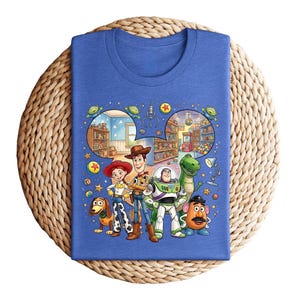 Pode incluir: Uma camiseta azul com um gr&aacute;fico colorido dos personagens de Toy Story. O design inclui Woody, Buzz Lightyear, Jessie, Rex, Sr. Batata, Slinky Dog e cenas do filme, para um visual divertido.