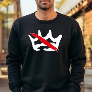 Peut inclure: Sweat-shirt noir &agrave; col rond avec un motif de couronne blanche barr&eacute;e d'une barre rouge. Le motif est centr&eacute; sur la poitrine. Le sweat-shirt est en mati&egrave;re souple.