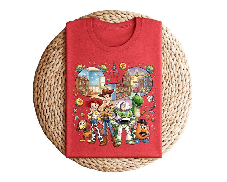 Pode incluir: Camiseta vermelha com um gr&aacute;fico colorido de personagens de Toy Story, incluindo Woody, Buzz Lightyear, Jessie, Rex, Sr. Batata e Slinky. O design incorpora cenas do filme. A camiseta est&aacute; dobrada sobre uma superf&iacute;cie tecida.