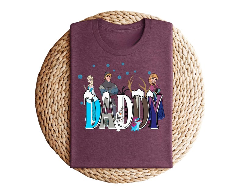 May include: A maroon t-shirt featuring the word "DADDY" in a stylized font with characters from the movie Frozen. The letters are decorated with snowflakes and images of Elsa, Anna, Kristoff, Olaf, and Sven.