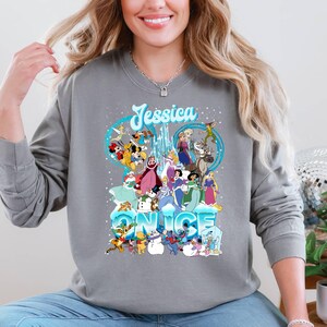 Puede incluir: Una sudadera gris con un gr&aacute;fico de personajes de Disney de Frozen y otras pel&iacute;culas de Disney. El texto "Jessica" y "Once" est&aacute; impreso en la sudadera.