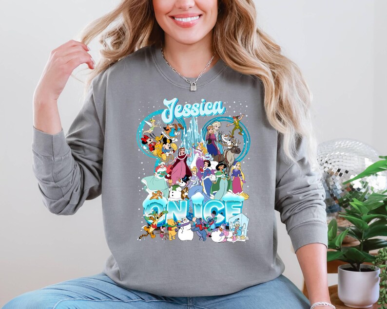 Puede incluir: Una sudadera gris con un gr&aacute;fico de personajes de Disney de Frozen y otras pel&iacute;culas de Disney. El texto "Jessica" y "Once" est&aacute; impreso en la sudadera.