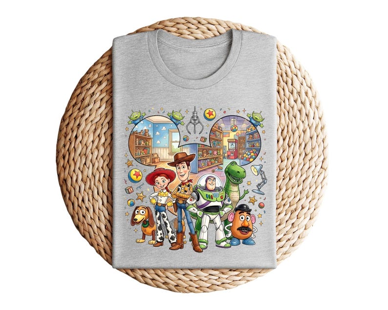 Pode incluir: Uma camiseta cinza claro com um gr&aacute;fico colorido de personagens da franquia de filmes Toy Story. O design inclui Woody, Buzz Lightyear, Jessie, Rex, Sr. Batata e Slinky Dog, junto com cenas de lojas de brinquedos.