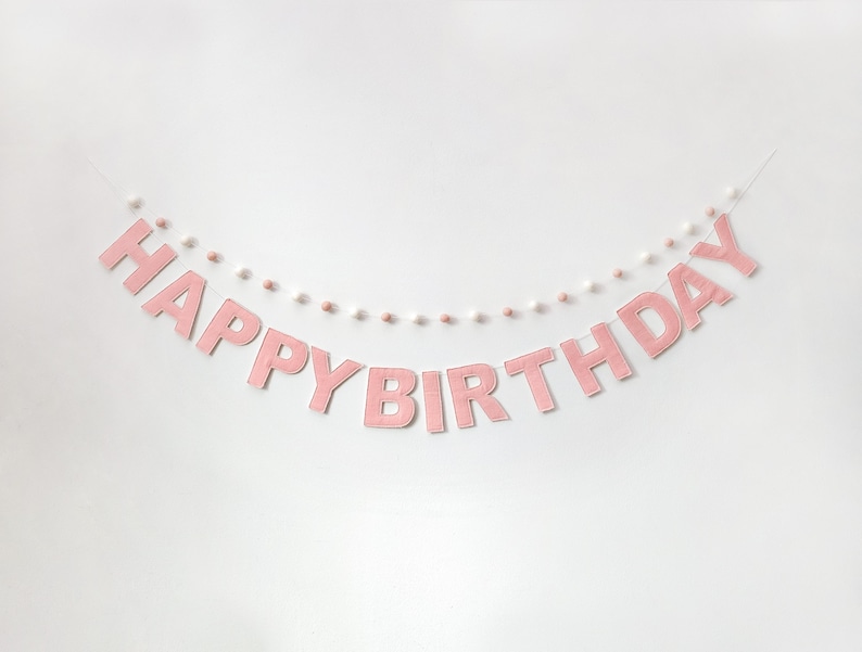 Pode incluir: Faixa de feltro rosa com pompons brancos que diz "Happy Birthday".
