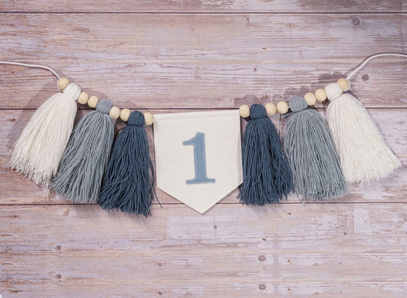 May include: A white banner with the number "1" in blue embroidery, strung with wooden beads and blue and white tassels.