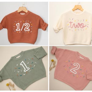 May include: Four different colored sweaters with embroidered numbers and sprinkles. The sweaters are in the colors clay terracotta, vanilla cream, dusty olive, and peachy pink.