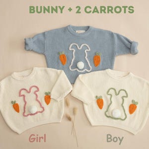 K&ouml;nnte beinhalten: Zwei wei&szlig;e Strickpullover mit gestickten Hasen- und Karottenmotiven. Ein Pullover hat einen rosa Hasen und der andere einen gr&uuml;nen Hasen. Der Text "Bunny + 2 Carrots" befindet sich oben im Bild. Der Text "Girl" befindet sich unter dem Pullover mit dem rosa Hasen und der Text "Boy" befindet sich unter dem Pullover mit dem gr&uuml;nen Hasen.