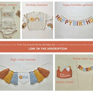 May include: A collection of birthday party decorations and apparel. Includes a cream-colored romper, a sweater, a garland, a high chair banner, a name crown, and a cake topper. The romper and sweater feature a sun and rainbow design. The garland says "HAPPY BIRTHDAY".