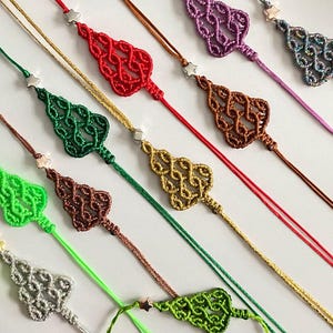 Puede incluir: Una colección de adornos de árbol de Navidad hechos a mano con macramé con cuentas de estrellas plateadas. Los adornos están hechos con cordones de diferentes colores, incluyendo rojo, verde, marrón, dorado y morado.