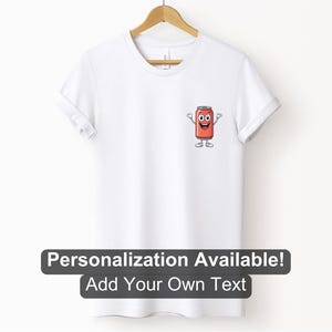 May include: A white t-shirt with a cartoon image of a red can with a smiling face and arms and legs. The text 'Personalization Available! Add Your Own Text' is below the image.