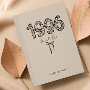 Może przedstawiać: Beżowy notatnik w twardej oprawie z rokiem 1996 w czarny wzór w panterkę, imieniem Michelle napisanym kursywą, małą ilustracją czarnej kokardki oraz napisem CHAPTER THIRTY wydrukowanym czarną czcionką na dole przedniej okładki.