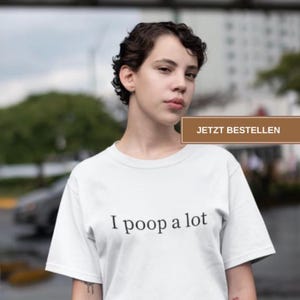 Könnte beinhalten: Weißes T-Shirt mit dem schwarzen Aufdruck "I poop a lot". Der Text ist zentriert. Das Bild zeigt eine Person mit kurzen, dunklen Haaren.