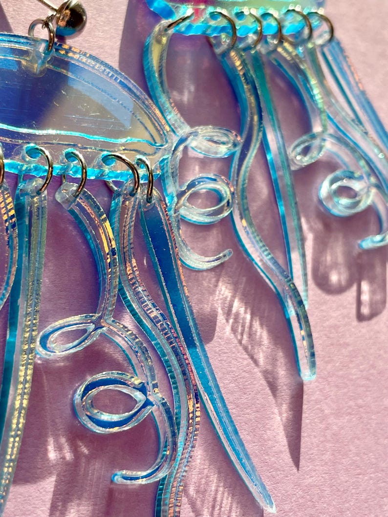 May include: Close-up of iridescent blue earrings with intricate, swirling designs. The earrings feature multiple layers and textures, with a mix of clear and colored elements. The design includes loops and dangling strands, creating a unique and eye-catching accessory.