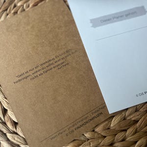 K&ouml;nnte beinhalten: Ein brauner Papierplaner mit dem Text "Geld ist nur ein Werkzeug. Es wird dich hinbringen, wohin du willst, aber es wird dich nicht als Fahrer ersetzen." - Ayn Rand. Der Planer hat den Text "Mein Planer, private Finanzen | Erstauflage &copy; Die Finanzkomplizen" unten.