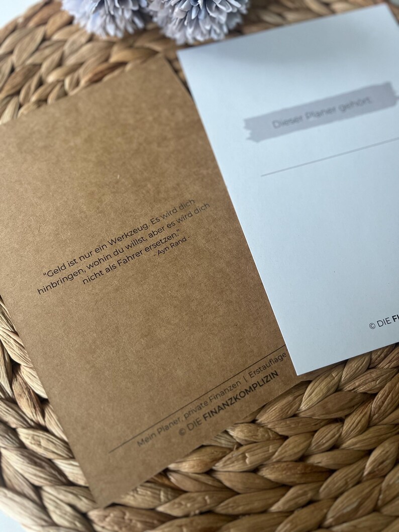 K&ouml;nnte beinhalten: Ein brauner Papierplaner mit dem Text "Geld ist nur ein Werkzeug. Es wird dich hinbringen, wohin du willst, aber es wird dich nicht als Fahrer ersetzen." - Ayn Rand. Der Planer hat den Text "Mein Planer, private Finanzen | Erstauflage &copy; Die Finanzkomplizen" unten.