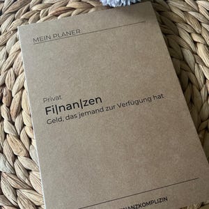 K&ouml;nnte beinhalten: Ein brauner Planer mit dem Text "Mein Planer" und "Privat Finanz" auf dem Cover. Der Text unter "Privat Finanz" lautet "Geld, das jemand zur Verf&uuml;gung hat". Am unteren Rand des Covers steht der Text "&copy; DIE FINANZKOMPLIZIN".