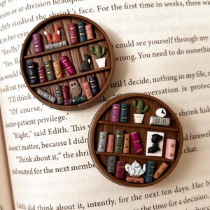 May include: Two round wooden shelf pins, each with miniature books, a fox, owl, cactus, and other decorative items. The pins are set on an open book.