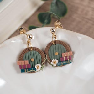 Op de afbeelding: Een paar groene deuroorbellen met bruine frames en een stapel boeken. De oorbellen zijn gemaakt van polymer clay en hebben gouden haakjes.