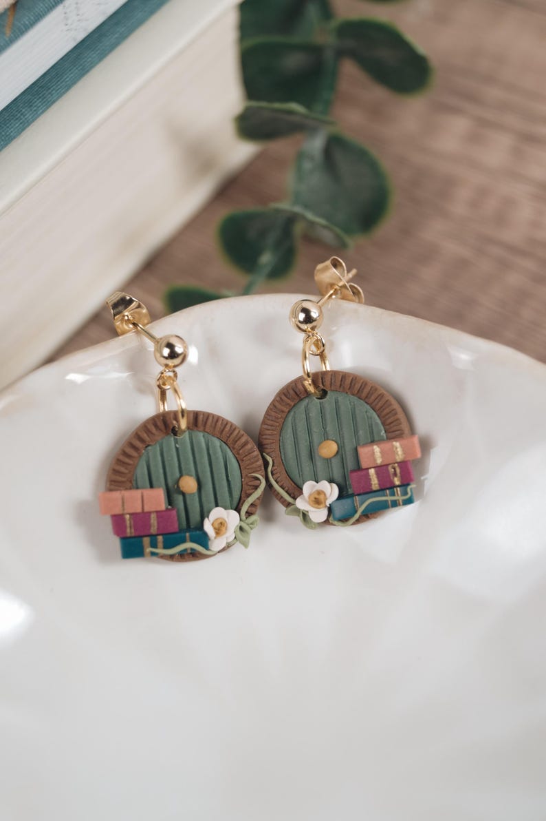 Op de afbeelding: Een paar groene deuroorbellen met bruine frames en een stapel boeken. De oorbellen zijn gemaakt van polymer clay en hebben gouden haakjes.
