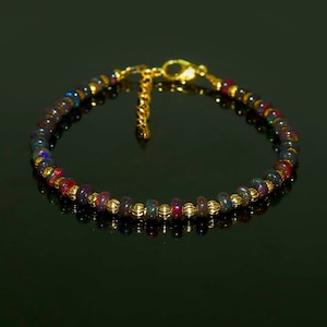 Peut inclure: Bracelet composé de perles d'opale foncées et irisées, alternant avec des entretoises dorées et un fermoir doré. Le bracelet est monté sur une chaîne dorée, créant un bijou délicat et élégant.