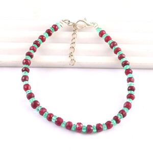 May include: A red and green gemstone bracelet with a silver clasp. The bracelet is made of small, faceted beads.