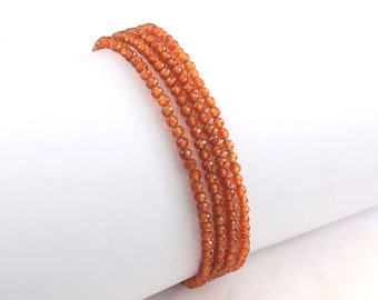 May include: A strand of orange gemstone beads. The beads are faceted and have a shiny finish. The strand is coiled on a white surface.