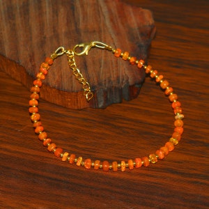 May include: A delicate orange opal beaded anklet with a gold clasp. The anklet is made of small, round beads that are strung together on a thin gold chain.