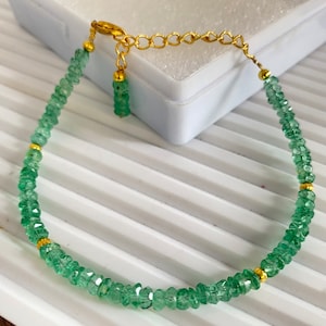 Puede incluir: Una delicada pulsera con pequeñas cuentas de esmeralda facetadas ensartadas con una cadena y detalles dorados. La pulsera tiene un cierre de mosquetón y una cadena ajustable. Las esmeraldas son de un color verde vibrante.