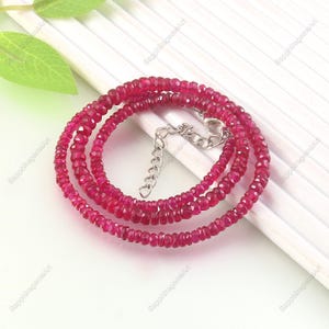 May include: A layered necklace made of small, faceted, ruby-coloured gemstones. The necklace has a silver-toned clasp and extender chain. The gemstones are strung together, forming a continuous loop of rich, red colour. This jewelry piece is suitable for various occasions.