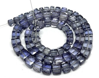 May include: A strand of faceted, cube-shaped beads in shades of blue and gray. The beads are strung together, creating a coiled pattern against a white background. The beads appear to be made of a translucent material.