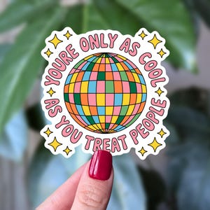 May include: A sticker featuring the text "YOU'RE ONLY AS COOL AS YOU TREAT PEOPLE" in pink, encircling a vibrant disco ball design. The disco ball is a grid of pink, yellow, green, and orange. The sticker has a white border with yellow star accents.