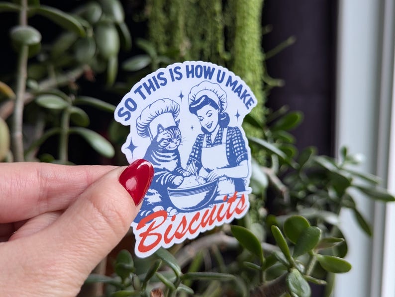 Puede incluir: Una pegatina azul y blanca con un gato de dibujos animados y una mujer con un gorro de cocinero. El texto de la pegatina dice "So this is how u make biscuits".