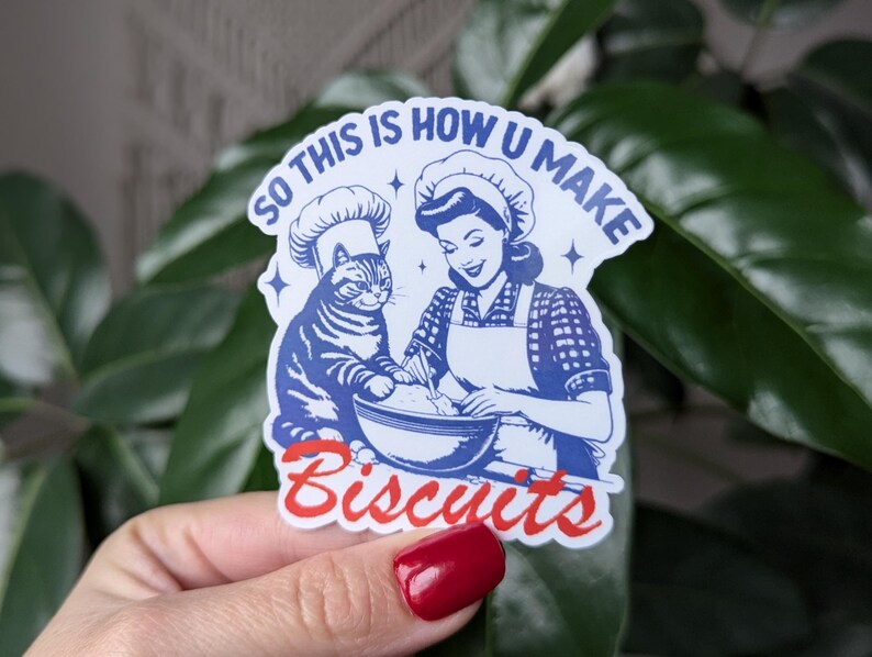 Puede incluir: Una pegatina azul y blanca con una ilustraci&oacute;n retro de una mujer y un gato haciendo galletas. El texto en la pegatina dice "So this is how you make biscuits".