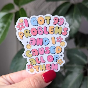 May include: A white sticker with colourful text that reads "I got 99 problems and I caused all of them". The text is in a retro font with flowers and smiley faces.